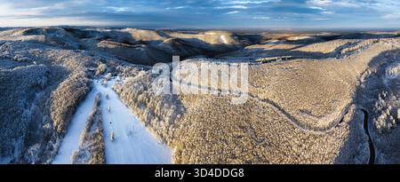 Aerial view of winter forest covered in snow at sunrise with road and ski slope Stock Photo