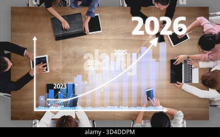 A diverse team of professionals engages in a strategic meeting, analyzing growth data and projections on digital devices while preparing for future Stock Photo