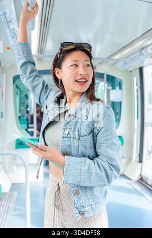 Young woman using smartphone and holding bar while standing on public transport. Stock Photo