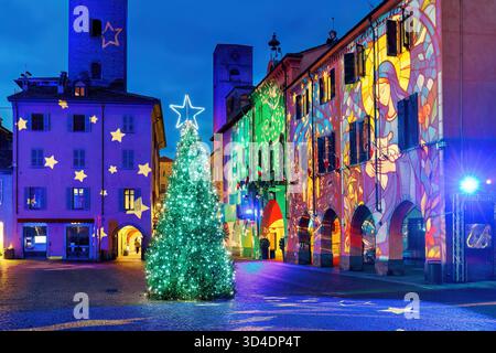 A sparkling Christmas tree stands on a cobbled town square surrounded by historic buildings, illuminated in the evening, in Alba, Italy. Stock Photo