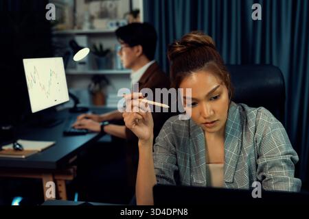 Serious face of thinking businesswoman focusing computer to report data analysis social media online project job with coworker working at back side at Stock Photo