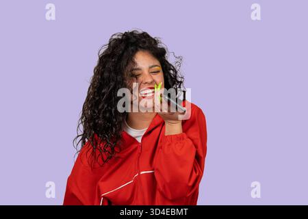Young woman laughing while recording a voice message on her mobile phone Stock Photo