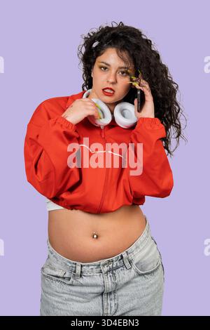 Young woman confidently communicating on phone, wearing 90s inspired fashion with headphones around her neck Stock Photo