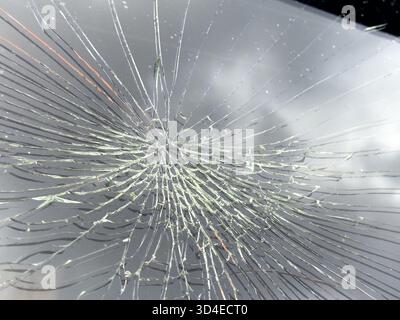 Shattered windshield with radiating cracks creating a spider web pattern on car surface, dramatic damage, accident scene, hazardous glass. Stock Photo