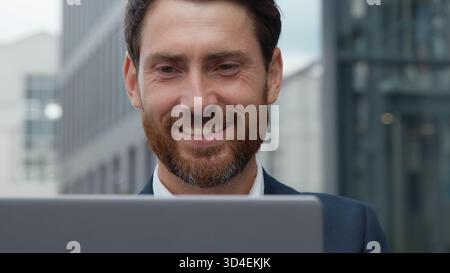 Close-up smiling handsome mature Caucasian business man looking at laptop in city smile toothy happy businessman male look at computer screen happy Stock Photo