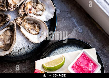 Fresh oysters presented on a dark plate with garnishes on the side Stock Photo