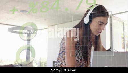 Leaning woman wearing patterned top and white headset typing on laptop in home office HUD overlays Stock Photo