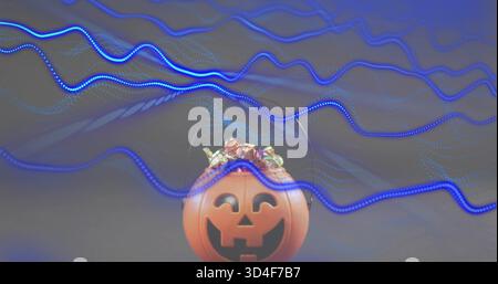 Sitting orange plastic jack-o'-lantern bucket holding wrapped candies on studio table, blue streaks Stock Photo