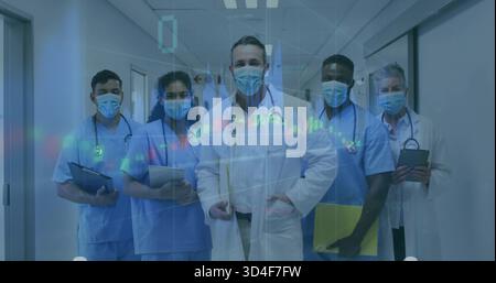 Standing med team posing in hospital corridor, wearing whitecoats or bluescrubs or masks, data overl Stock Photo