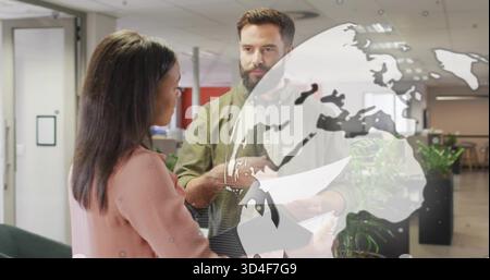 Explaining bearded man holding papers and pink blazer woman holding tablet in office, globe overlay Stock Photo