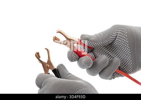 A gray gloves holding opened alligator clip handles with cables, one red and one black, on white background. image focuses on tools Stock Photo