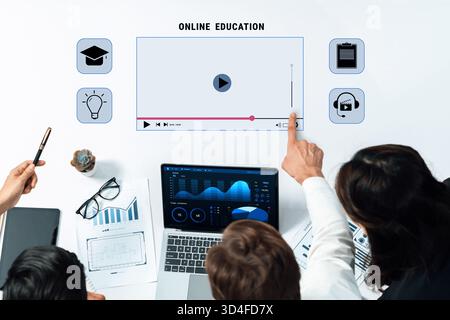 A diverse group discusses online education strategies using a laptop and interactive screen, emphasizing teamwork and innovative learning methods in a Stock Photo