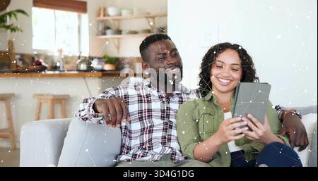 Sharing tablet, man in plaid shirt and woman in olive shirt sitting on couch in kitchen Stock Photo