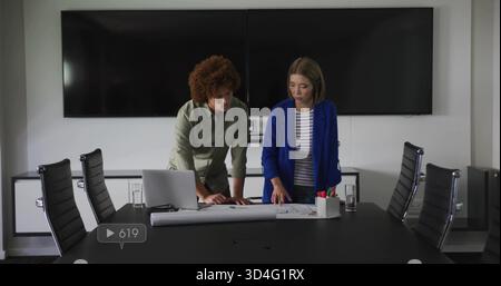 Checking two business architects examining blueprints on boardroom table silver laptop, markers Stock Photo