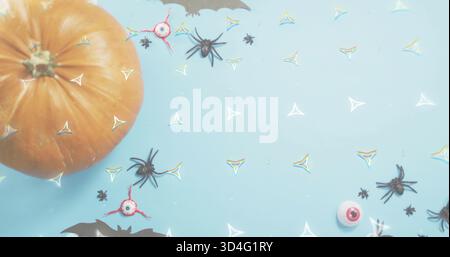 Positioning orange pumpkin left on pale-blue table scattering spiders eyeballs confetti, copy space Stock Photo