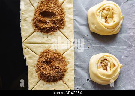 Making cinnamon rolls, dough lies on baking sheet, divided into squares, filling poured in, round buns formed, top view Stock Photo