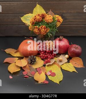 Autumn still life with marigold bouquet, pumpkin, apples, pomegranate, berries and colorful leaves on dark rustic background. Stock Photo