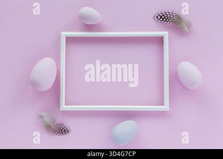 Minimalistic Easter holiday background with pastel colored eggs, photo frame and feathers on a pink background. Flat lay greeting card with space for Stock Photo