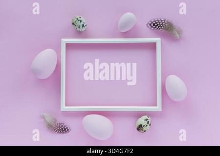 Minimalistic Easter holiday background with pastel colored eggs, quail eggs, photo frame and feathers on a pink background. Flat lay greeting card wit Stock Photo