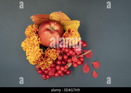 Autumn still life with apple, marigold flowers, red berries and colorful leaves arranged in a small basket on dark background. Stock Photo