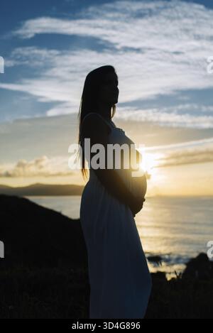 Silhouette of a pregnant woman against an oceanic landscape in Galicia, Spain Stock Photo