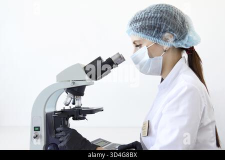 Female scientist looking through microscope in modern chemical laboratory doing some research. Analyzing samples using microscope Stock Photo
