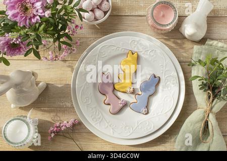 Food, Easter spring table setting. White plate with colorful royal icing bunny cookies. Flat lay. Wooden background, top view Stock Photo