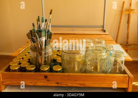 potbelly pig. Art supplies are neatly arranged on a wooden table, featuring jars filled with brushes and various containers for creative endeavors Stock Photo