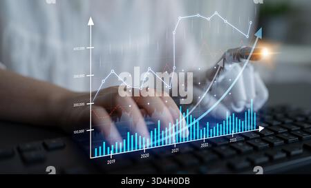 A focused data analyst interacts with financial graphs while typing on a keyboard, representing modern technology use in business analytics and Stock Photo