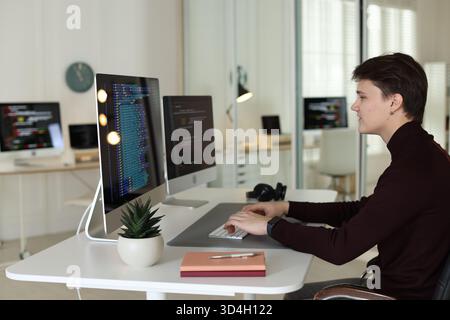 Programmer working on computer with dual monitors at white table in office Stock Photo