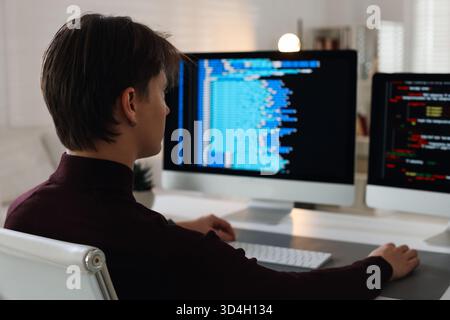Programmer working on computer with dual monitors at white table in office Stock Photo