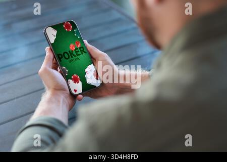 Man playing online poker on mobile phone at table, closeup Stock Photo