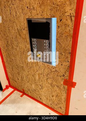 Elevator control panel mounted in a temporary OSB construction wall, marked with red tape for protection and renovation work. This image is ideal for Stock Photo