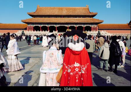 Inside the Forbidden City — visitors in colorful traditional attires cross the main courtyard toward a grand palace hall Stock Photo