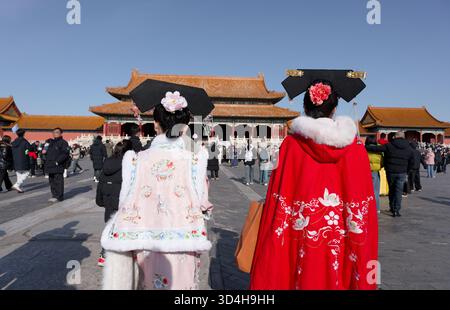 Two visitors in embroidered winter hanfu stop to admire the palace halls inside the Forbidden City Stock Photo