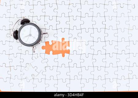 Alarm clock over missing puzzle piece suggests urgency, highlighting time's role in completing tasks or solving unresolved problems. Stock Photo