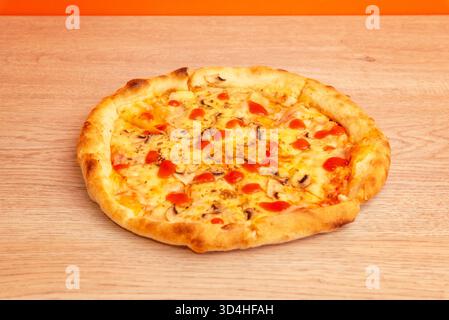 Hot pizza with tomato sauce and melted cheese on wooden table in cozy kitchen interior, blurred background bottles of olive oil Stock Photo