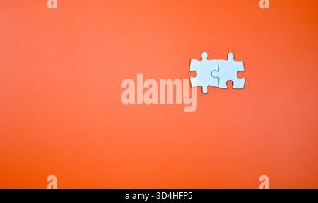 Two interlocked white puzzle pieces on orange background, symbolizing connection, unity, or problem-solving in a minimal visual composition. Stock Photo