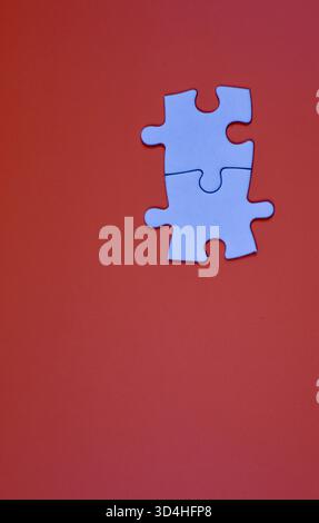 Two interlocked white puzzle pieces on orange background, symbolizing connection, unity, or problem-solving in a minimal visual composition. Stock Photo