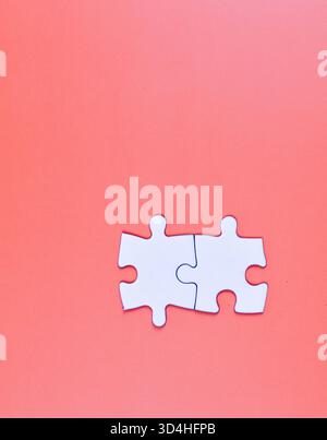 Two interlocked white puzzle pieces on orange background, symbolizing connection, unity, or problem-solving in a minimal visual composition. Stock Photo
