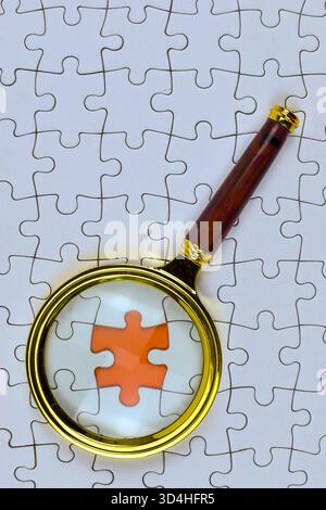 Magnifying glass highlights orange puzzle piece among white pieces, emphasizing focus, uniqueness, and detailed problem-solving within uniform structu Stock Photo