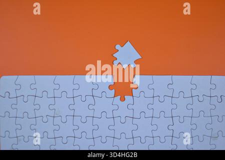 White jigsaw puzzle on orange background with one piece missing and nearby, symbolizing final step toward visual and structural completion. Stock Photo