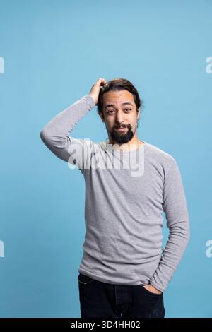 Middle eastern uncertain person feeling unsure and confused against blue background, contemplating and feeling curious in studio. Young adult acting thoughtful and reflective, decision making. Stock Photo