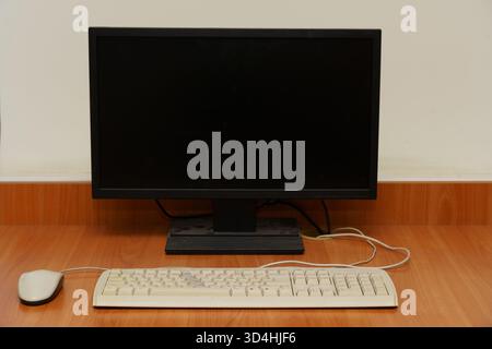 A computer sits quietly on a wooden desk, featuring a monitor, keyboard, and mouse, ready for use in an office space. Stock Photo