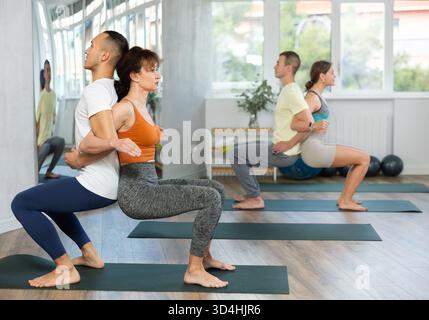 Group of men and women doing acroyoga exercises in pairs, exercising partner yoga during training in fitness center Stock Photo