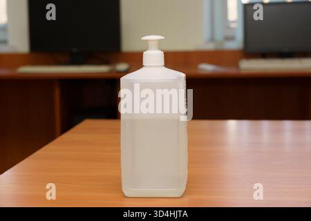 Hand sanitizer bottle placed on a wooden table in a well-lit office environment Stock Photo