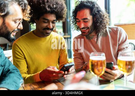 Friends drinking beer and using smartphone in bar Stock Photo