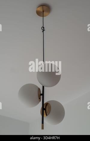 Three matte opal globes encircle a slim black rod with brass accents in a bright Gdansk apartment, shot upward with soft daylight that shapes a calm s Stock Photo