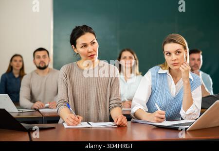 Students writing in notebook and typing on laptop during class in classroom Stock Photo