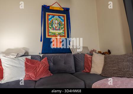 Charcoal gray sectional with pillows and throw sits below a Tibetan style thangka. Warm natural light, tight framing, and soft textures create intimat Stock Photo